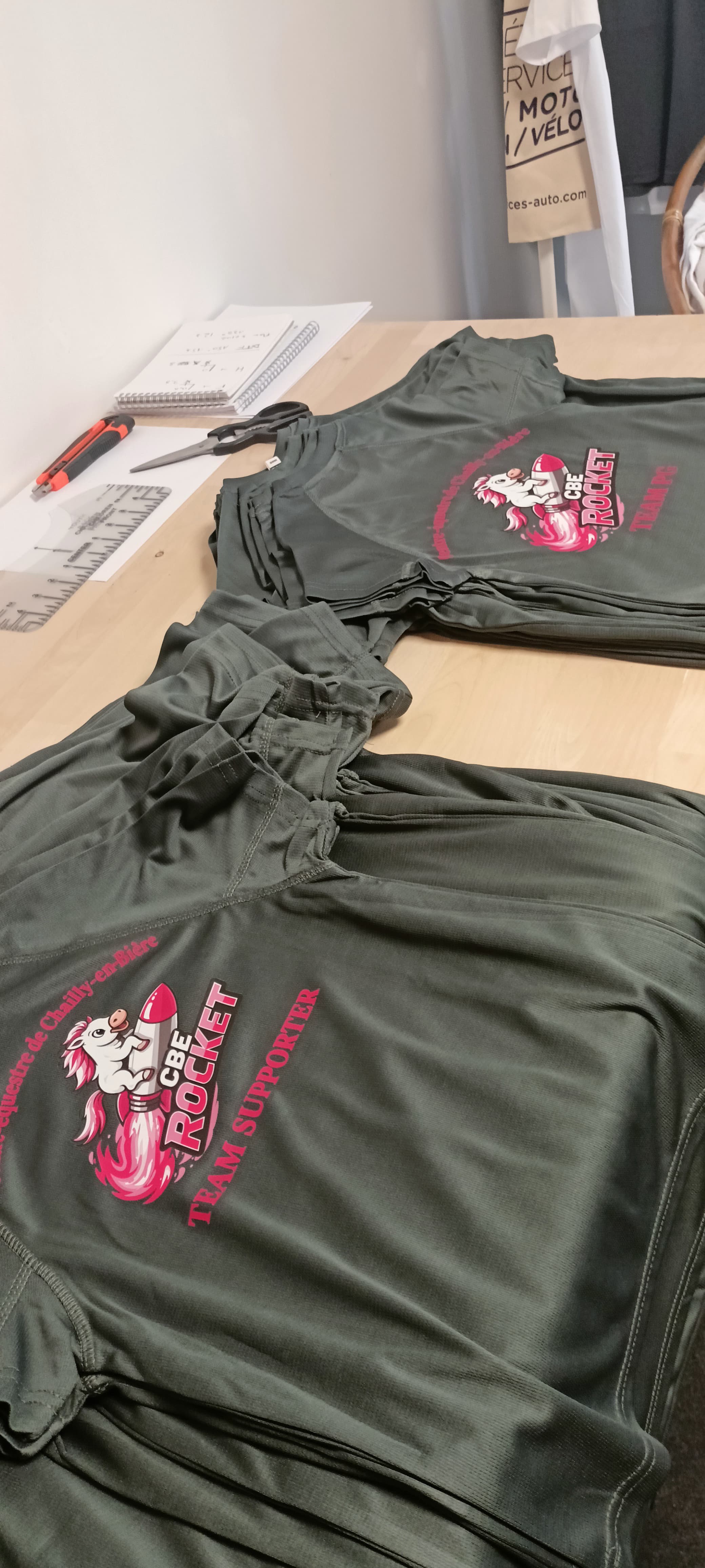Plusieurs T-shirts de sport du poney-club disposés sur la table de l’atelier